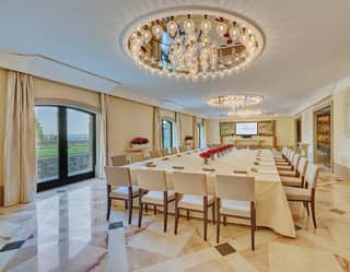 Large banquet table set for a meeting in a marble-tiled bright and airy room