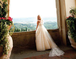 Bride in a wedding dress leaning against a stone arch with views of the hills of Fiesole