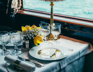 Yellow lilies and white gypsophilia decorate an elegant window dining table with views of Lake Geneva and the Alps