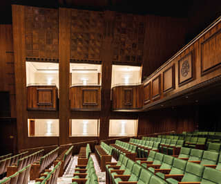 Spacious walnut wood-panelled theatre with rows of green chairs and balcony seating