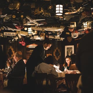 Guests at tables in a dark-lit restaurant with an eclectic collection of ceiling ornaments