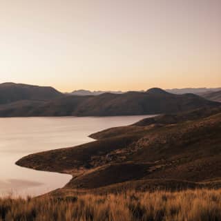 A sunset view of Lake Saracocha with its tranquil waters and soft contours bathed in golden hues.