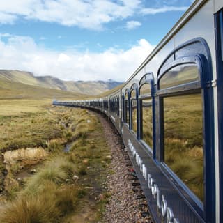 Row of train windows reflecting the lush Andean plains trackside