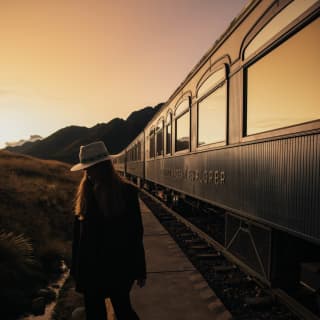 A woman with a fedora hat standing near the Andean Explorer at sunset