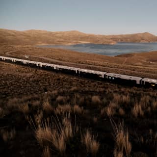 High angle view of the white and maroon carriages as the Andean Explorer files through the russet grasses by Lake Saracocha.