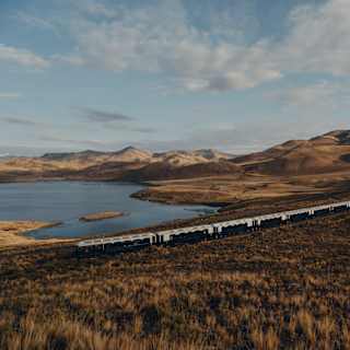 The train travels through russet grasslands overlooking the curves and contours of Lake Lagunillas, seen from a hill above.