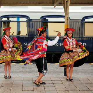 Four Peruvian dancers in traditional dress whirling on a train platform