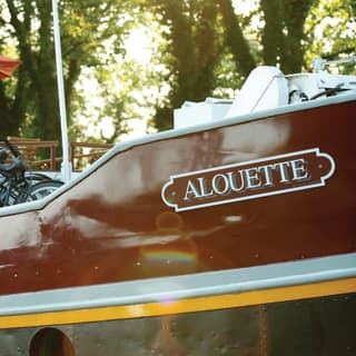 Gros plan sur une péniche de luxe appelée Alouette, sur un canal bordé d'arbres