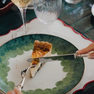 A guest cuts into a slice of quiche with a perfectly browned top and crisp pastry, on a green and white china plate.