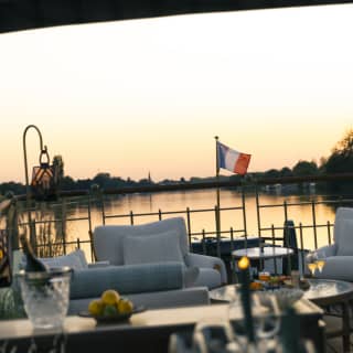 Looking over a dining table in soft-focus to the seating area, where a small French flag flies against the peachy sunset sky.