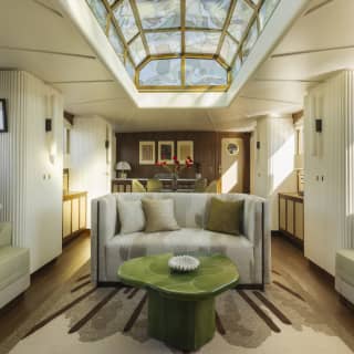 A glass ceiling lantern spills light into the lounge, furnished with sage and soft grey banquettes and sofa, with wood fittings.