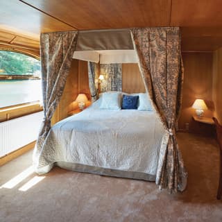 Sunlight-filled wood-panelled cabin with a plush four-poster bed and toile drapes