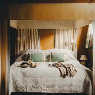 A double cabin with mellow ambience, comprising a four-poster bed with a white quilt, mint-green cushions and reading lamps.