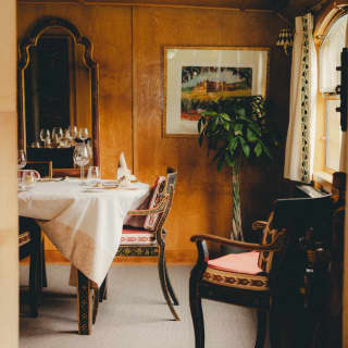 The light-filled dining room, with walnut panelling, mirror, vintage carver-style chairs and a table laid for fine dining.