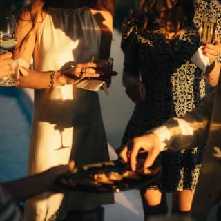 Stylishly-dressed guests mingle on deck in the golden evening sun with drinks, while platters of nibbles are passed around.