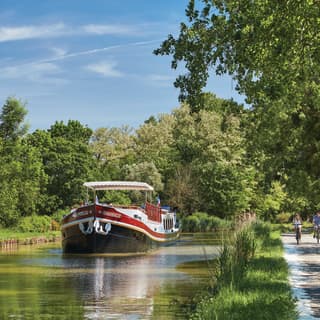 Black bottomed river barge with a red stripe drifting down a tree-lined canalside