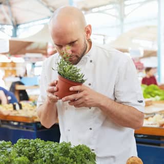 Chef in chef whites smelling fresh herbs in a little pot from a food market