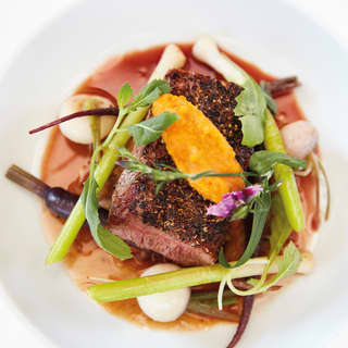Birds-eye-view of a braised steak dish topped with an orange and spring onion salad
