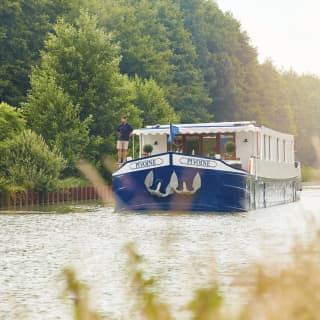 Blue bottomed luxurious river barge sailing along a tree-lined river