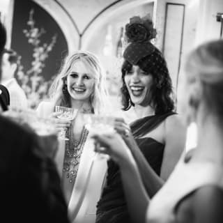 In black and white, four friends in formal evening dress smile and laugh as they raise a toast in a vibrant party