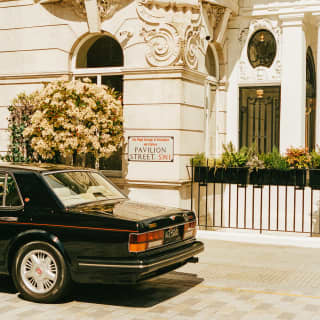 The back of a black 1990s Bentley, parked outside the portland stone, ground-floor edifice of The Cadogan on Pavilion Street.
