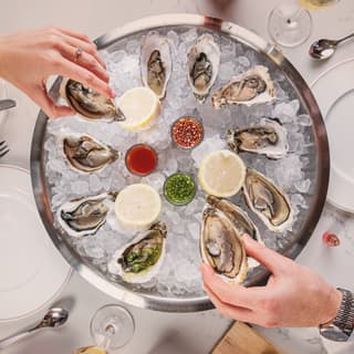 Twelve Porthilly oysters are served on a silver ice platter with lemons and ramekins of shallot vinegar and cucumber dressing