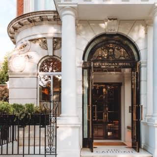 Beneath a white stone portico, The Cadogan Hotel's logoed wood and glass doors open to a glimpse of the gleaming interior.