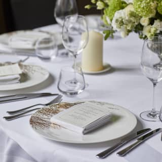Close-up of a setting at a wedding dinner with a personalised card in the centre of a porcelain plate with a twig pattern.