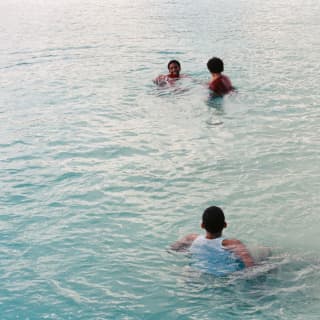 Three boys play in the calm, soft blue waters by Cap Juluca resort as a gentle sun shimmers on the surface.