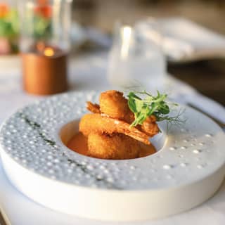 A small deep plate with a wide rim and deep centred well holds three giant breaded prawns in a mango chipotle sauce