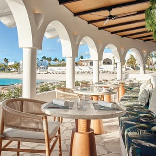 A row of circular tables on a curved restaurant terrace over the beach