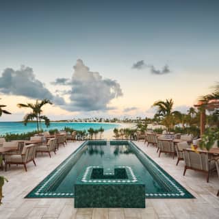 A long and narrow pool tiled in emerald green points to the beach, flanked by rows of rosewood tables and cushioned armchairs