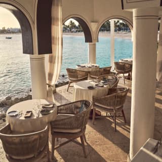 High-angle view of the colonnaded terrace at Pimms where round tables and wicker chairs are placed for dinner with bay views.