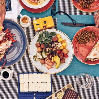 Birds-eye-view of hands reaching for cooked crabs on a dish surrounded by salads and light bites