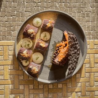 A chocolate mousse dessert with vanilla cream, hazelnut, and pisco ice cream, presented on a stone plate, seen from above.