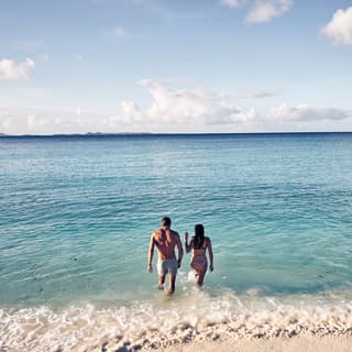 A couple strolling from the shore into the calm turquoise sea before them