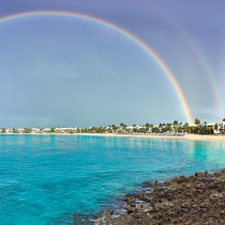 A rainbow in blue skies over the turquoise water of Maundays Bay