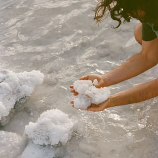 Close-up of hands holding snowball-like, white, crystalised salt at the lake's edge during a harvesting.