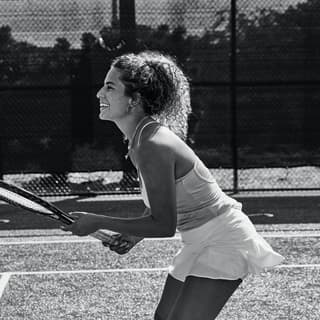 A smiling lady in a tennis outfit holding a racquet and preparing for a return shot