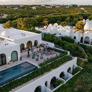 Aerial view of a yoga class, as guests stands on their mats on a second-floor terrace alongside an infinity pool.