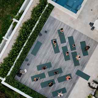 Bird's-eye view of a yoga class with twelve participants on the spa deck by an infinity pool in the lush resort surrounds.