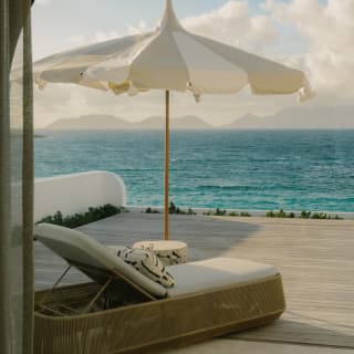 A luxurious sun lounger reclines beneath a pointed parasol on the pool terrace of the Spa by Guerlain, overlooking the bay.