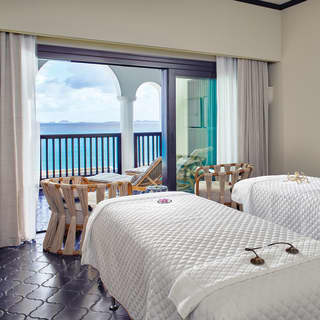 Twin massage couches draped in white face the open patio doors, looking out across the tiled terrace to the azure sea