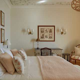 View over a bedroom in Villa Margherita with a large bed and furnishings in pink and cream florals, with vintage furniture.