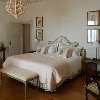 A tangle-design light pendant hangs above the bed, with soft pink throw and subtle floral cushions, in a view of the bedroom.