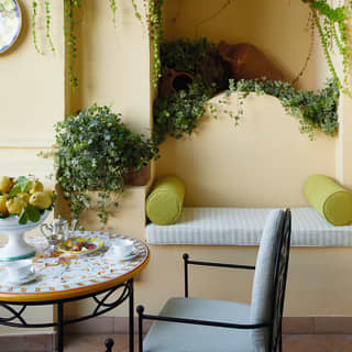 A small lime green bolster sits on a bench seat, hugging the edge of a Naples yellow wall, next to coffee table with espresso
