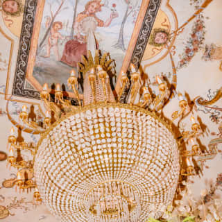 A large crystal chandelier hangs below an ornate and colourful fresco of flowers and mythical gods
