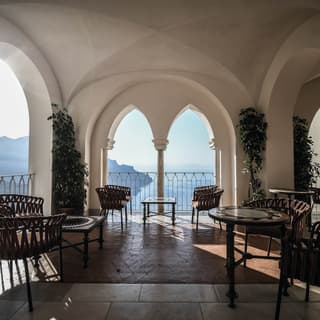 Bar tables on an open-air stone terrace with arched windows overlooking the Amalfi Coast