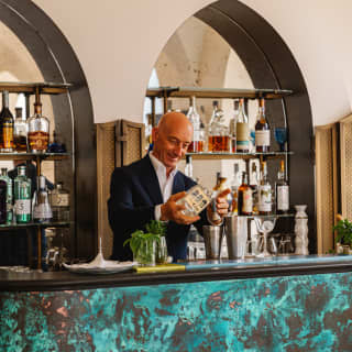 The bartender mixes drinks at Caruso's bar, with a dramatic turquoise and black surface and arched shelving alcoves behind.