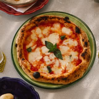 A stone-baked pizza with delicious crispy dough, rich tomato sauce and oozing mozzarella with basil garnish, seen from above.